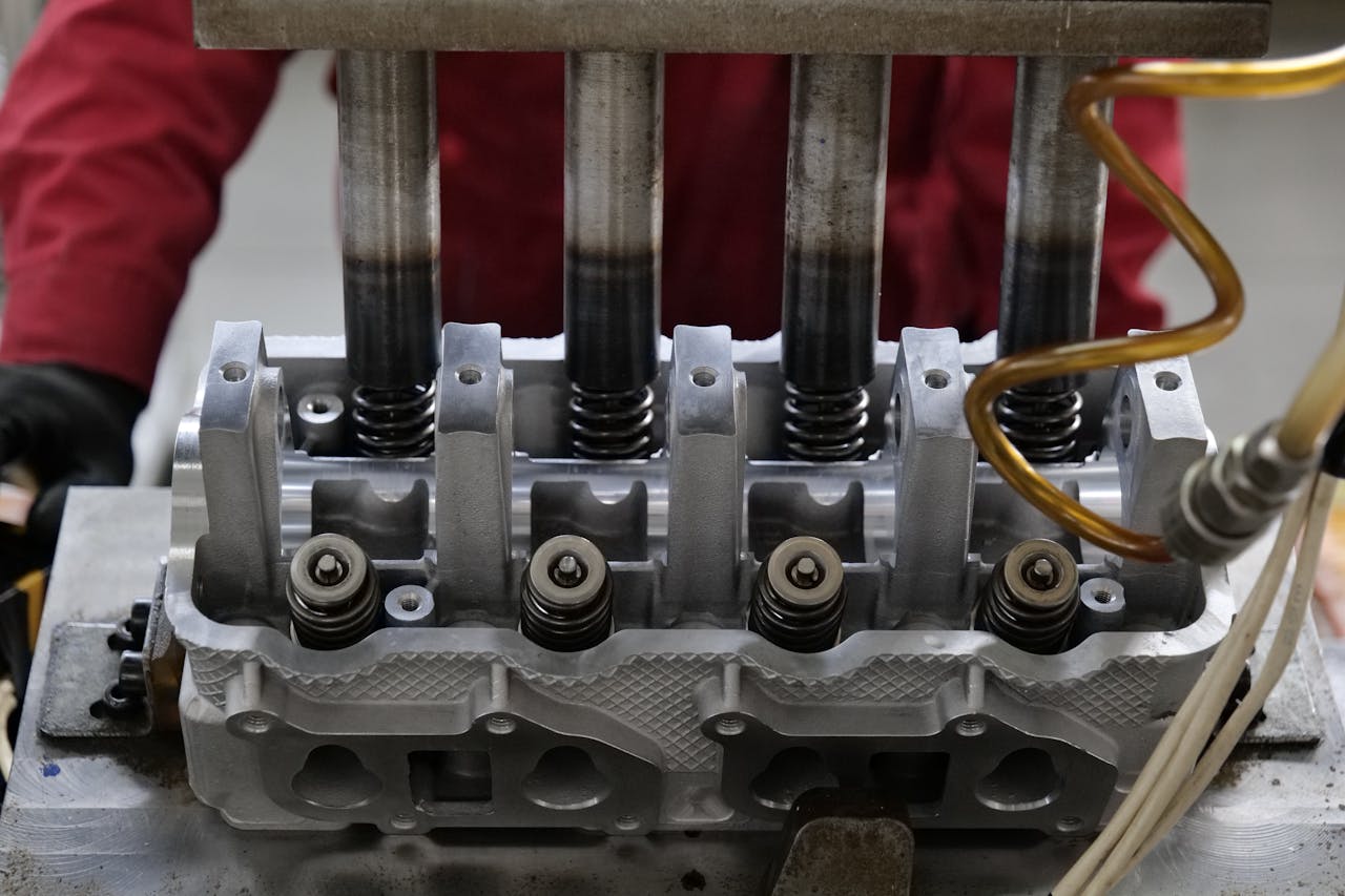 Detailed view of a metallic engine cylinder head with springs and pistons, assembled in an industrial workshop.